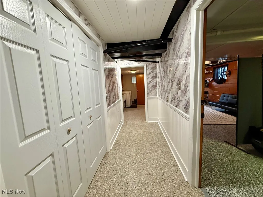 Hallway with a wainscoted wall and light colored carpet