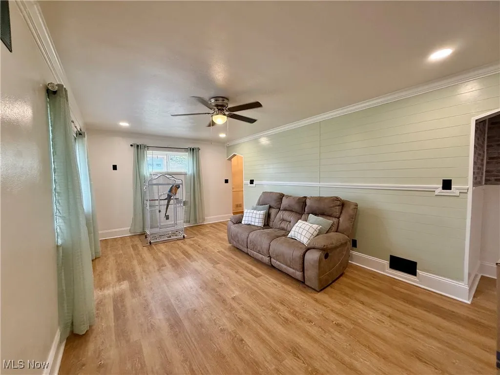 Living room with ornamental molding, light wood -style flooring, arched walkways, ceiling fan, and wooden walls