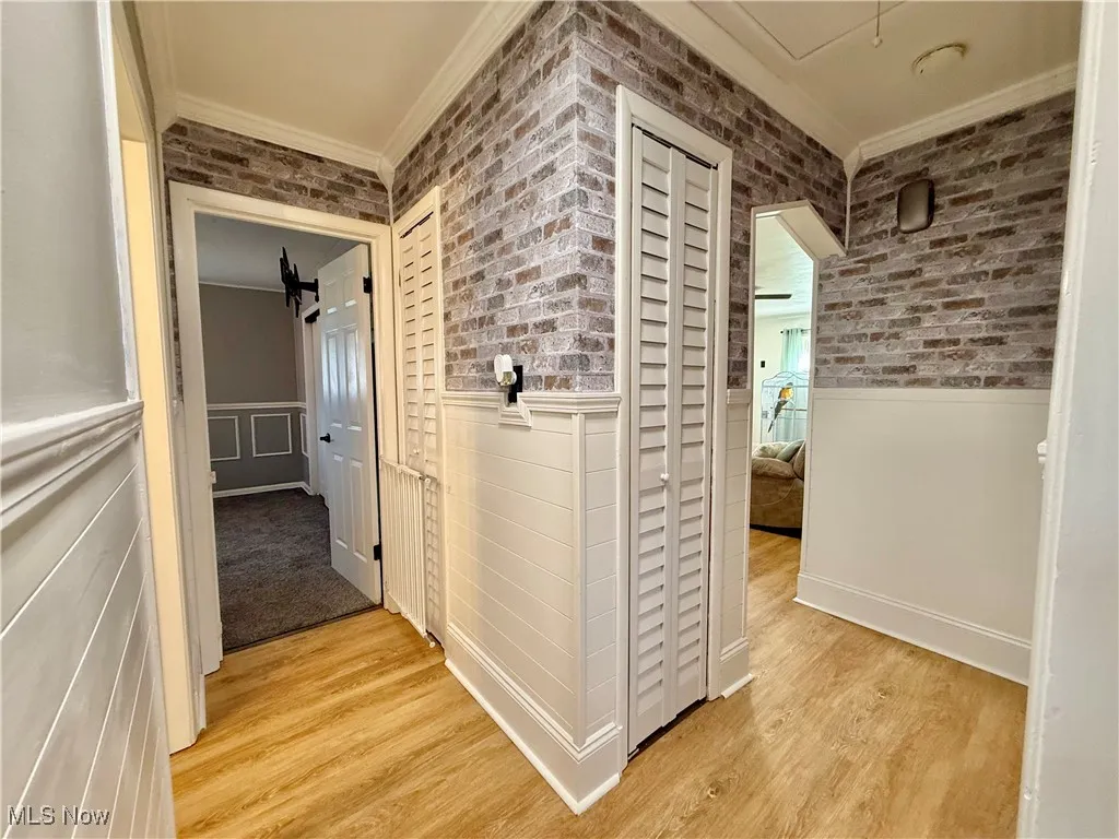 Hall featuring ornamental molding, brick wall, light wood-style floors, attic access, and wainscoting