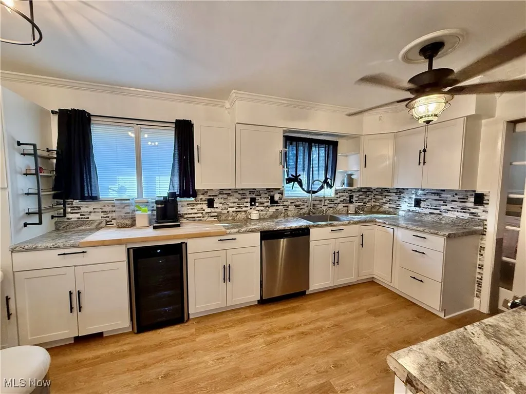 Kitchen with white cabinetry, beverage cooler, backsplash, stainless steel dishwasher, and ornamental molding