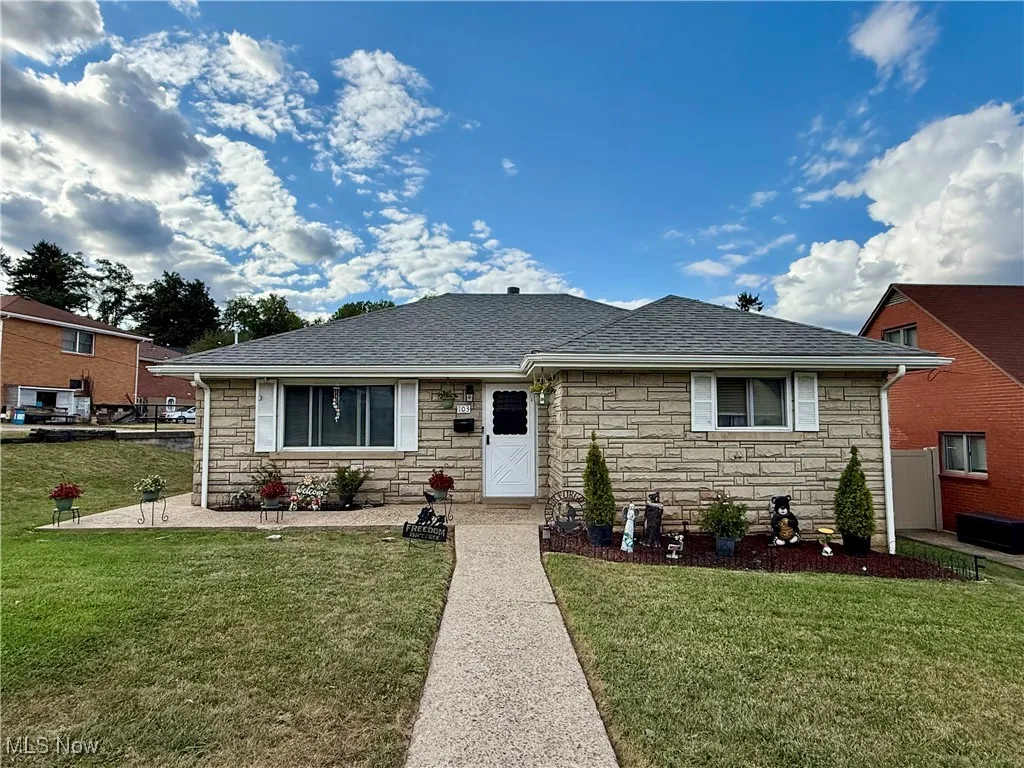 View of front of property with stone siding, a front yard, and a shingled roof