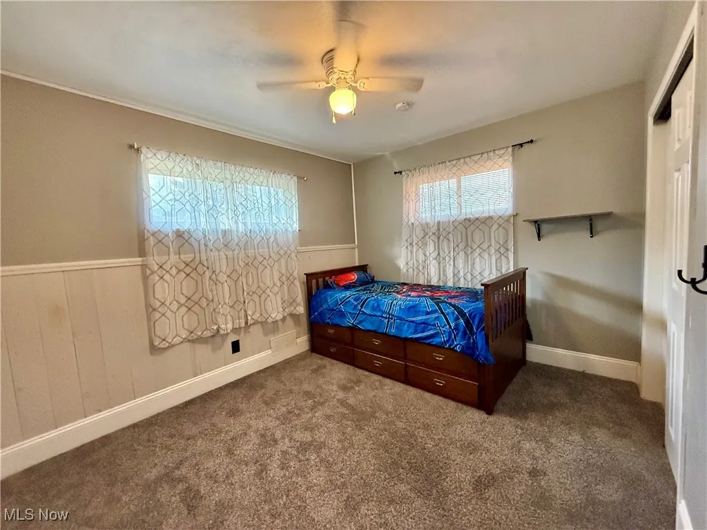 Bedroom with multiple windows, a ceiling fan, carpet floors, wainscoting, and wood walls