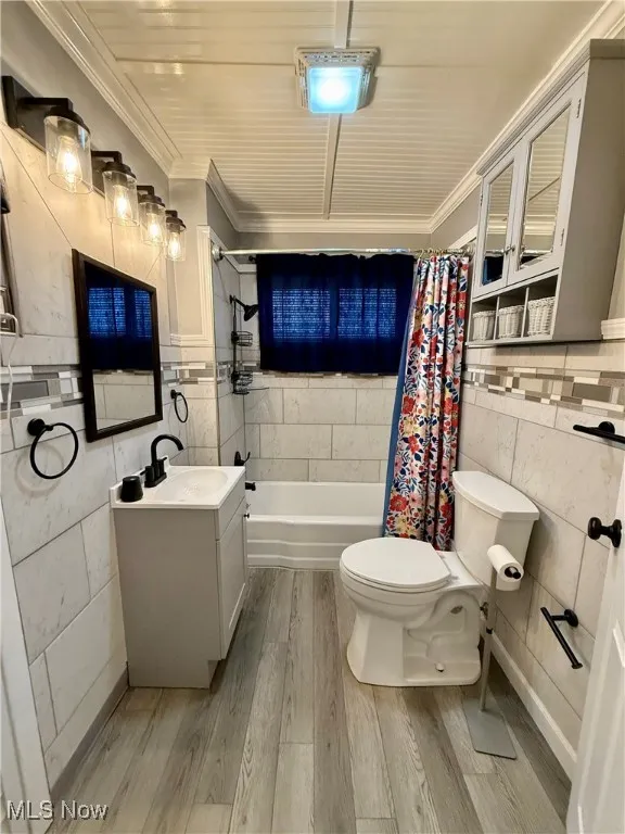 Bathroom with tile walls, shower / bathtub combination with curtain, light wood-style flooring, vanity, and crown molding