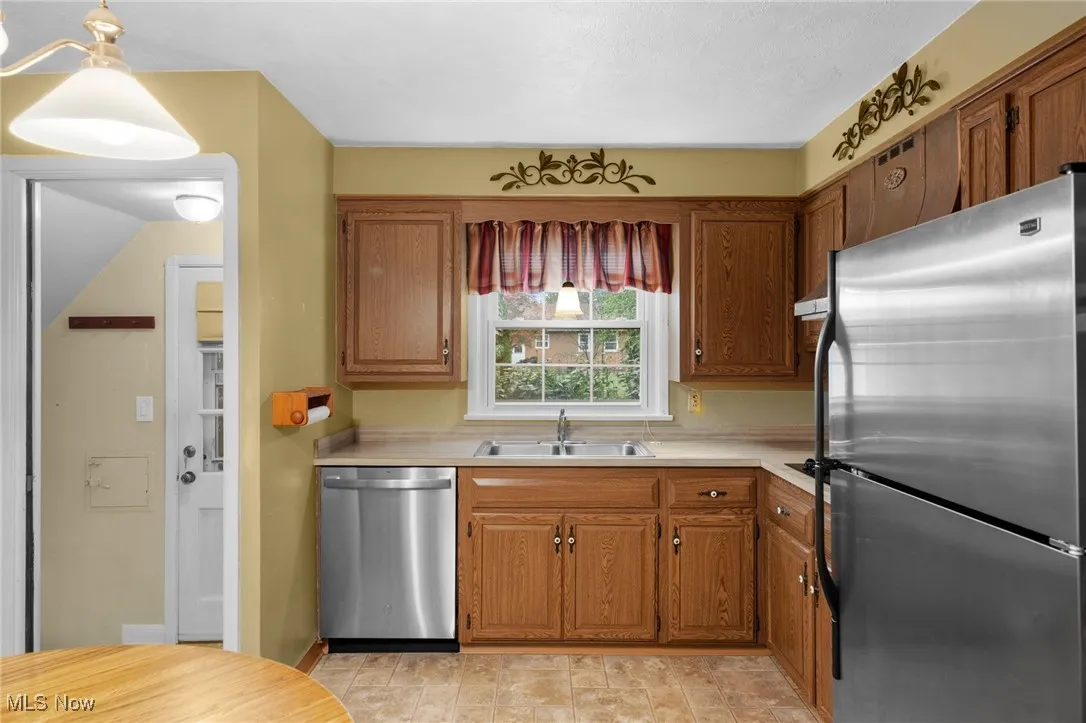 Kitchen featuring stainless steel appliances, light countertops, brown cabinetry, and pendant lighting