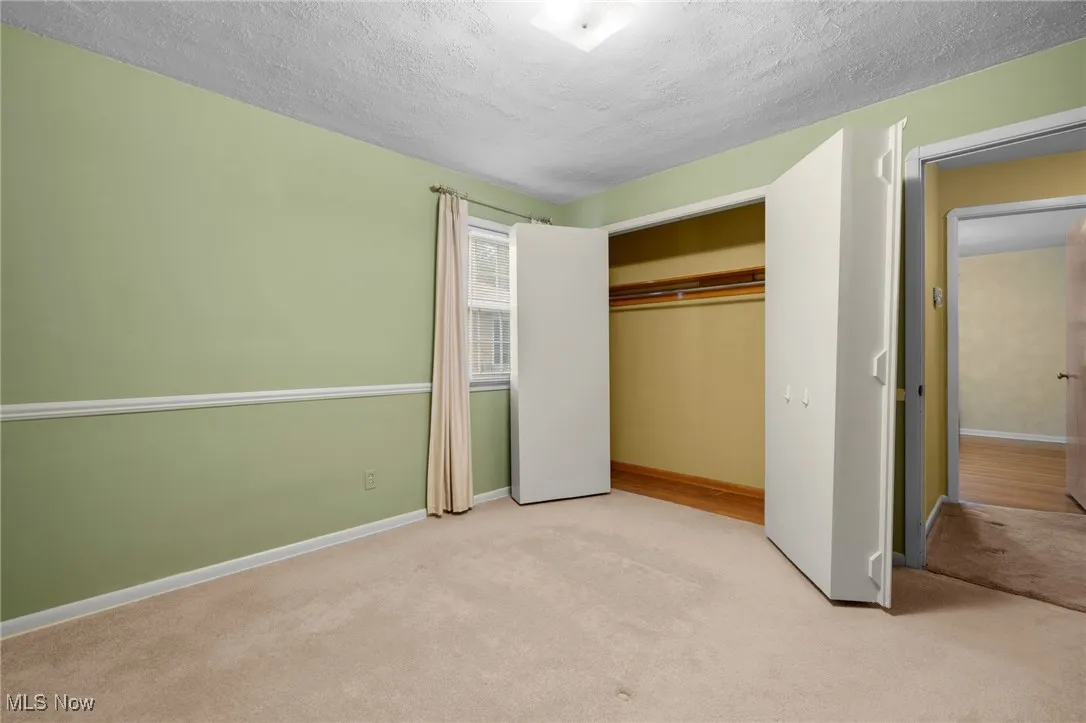 Unfurnished bedroom with light colored carpet, a closet, and a textured ceiling