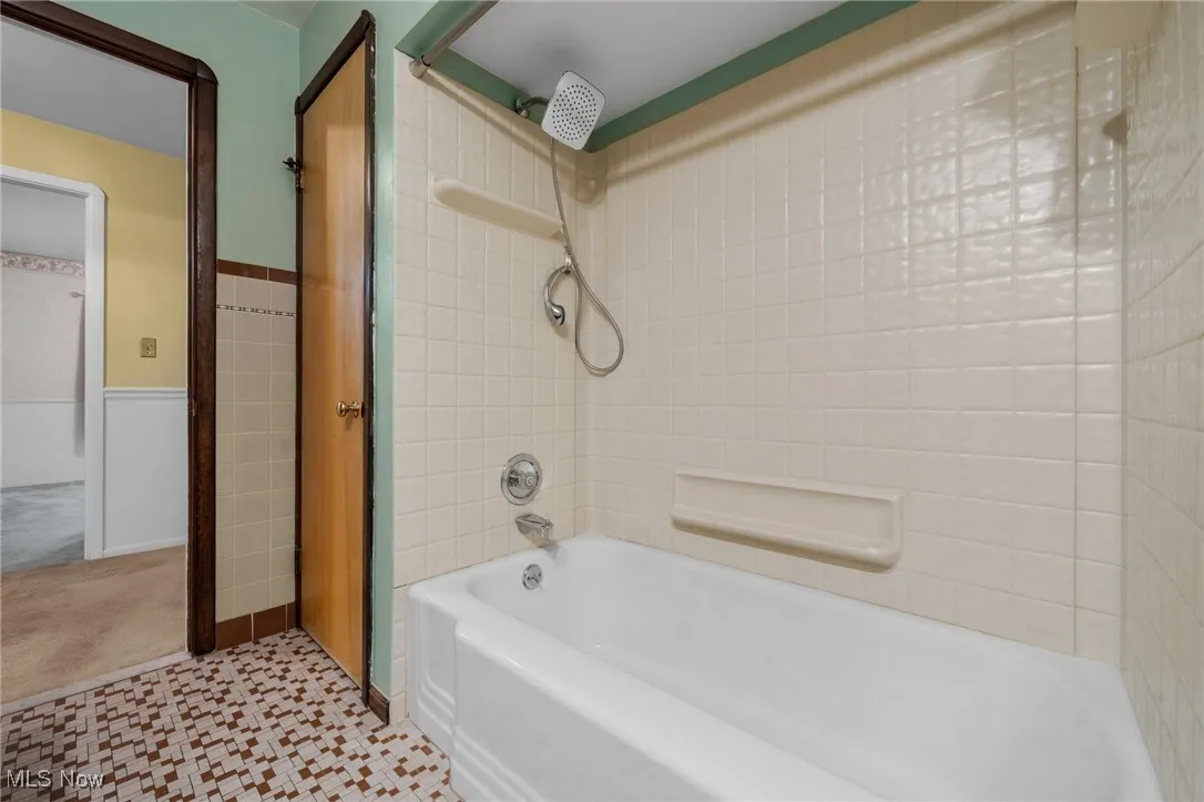 Bathroom featuring shower / tub combination, tile walls, wainscoting, and tile patterned floors