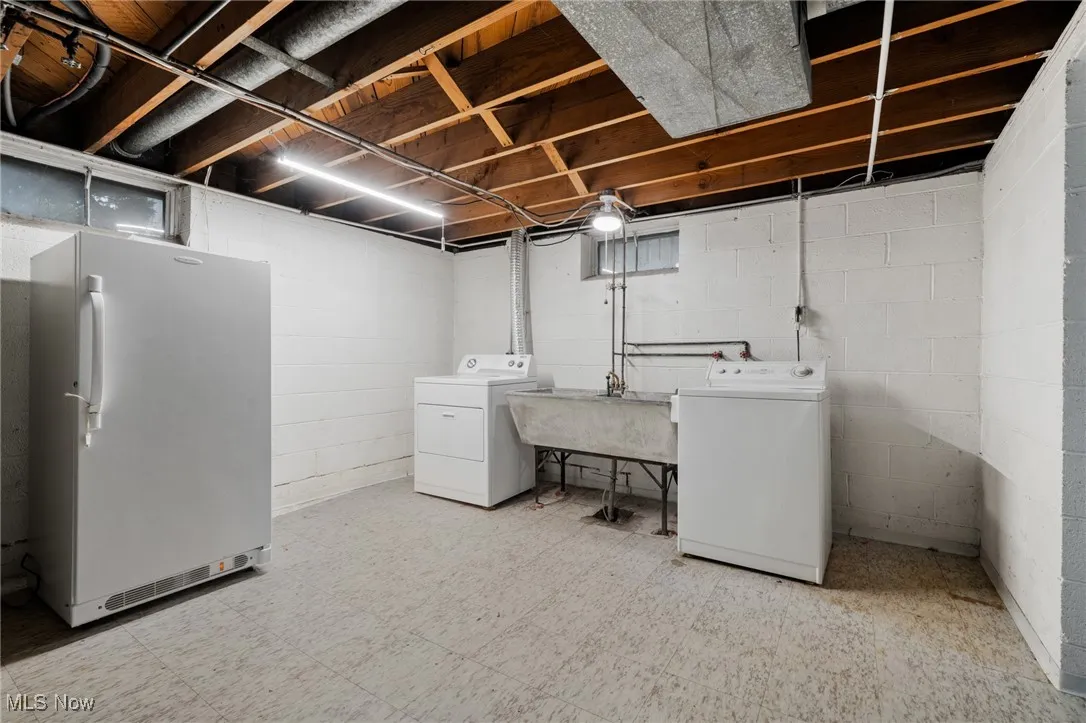 Unfinished below grade area with tile patterned floors, freestanding refrigerator, and washer and clothes dryer