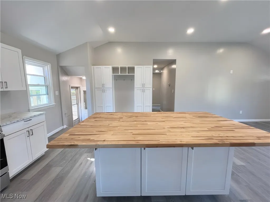Kitchen featuring vaulted ceiling, wood finished floors, white cabinetry, a kitchen island, and butcher block counters