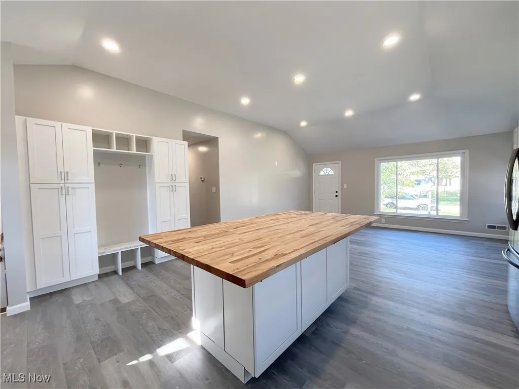 Kitchen with lofted ceiling, wood counters, white cabinetry, a center island, and recessed lighting
