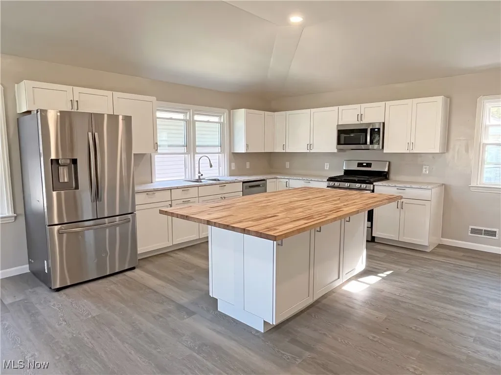Kitchen featuring stainless steel appliances, butcher block countertops, white cabinetry, a center island, and light wood-type flooring