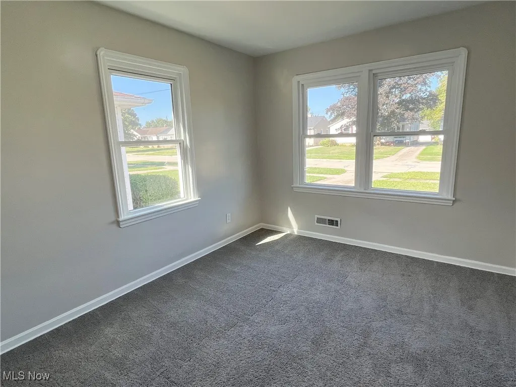 Spare room featuring dark colored carpet and baseboards