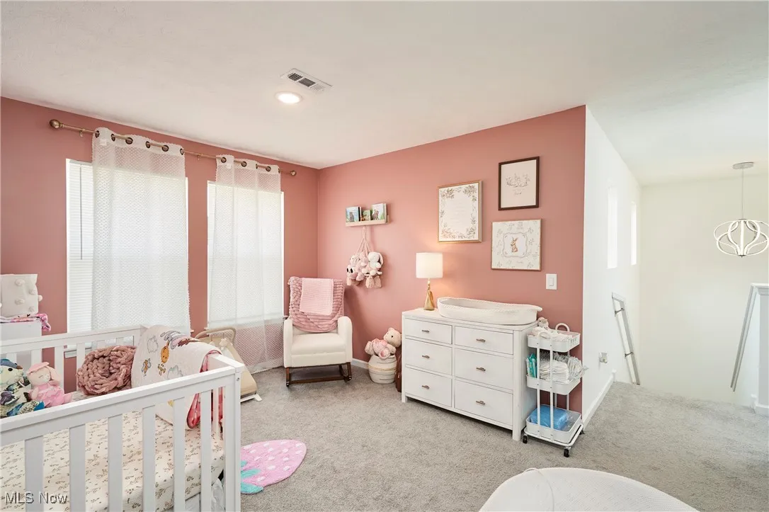 Bedroom with a crib, light colored carpet, and a chandelier