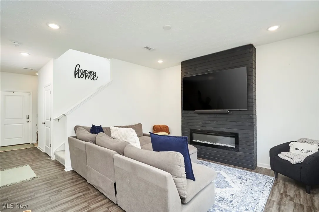 Living room featuring a large fireplace, lvp wood finished floors, recessed lighting, and stairway