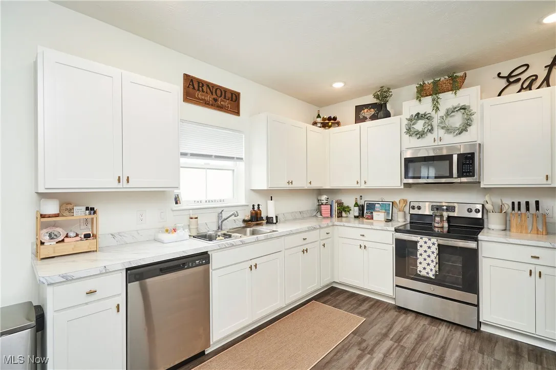 Kitchen with appliances with stainless steel finishes, white cabinetry, LVP wood finished floors, and recessed lighting