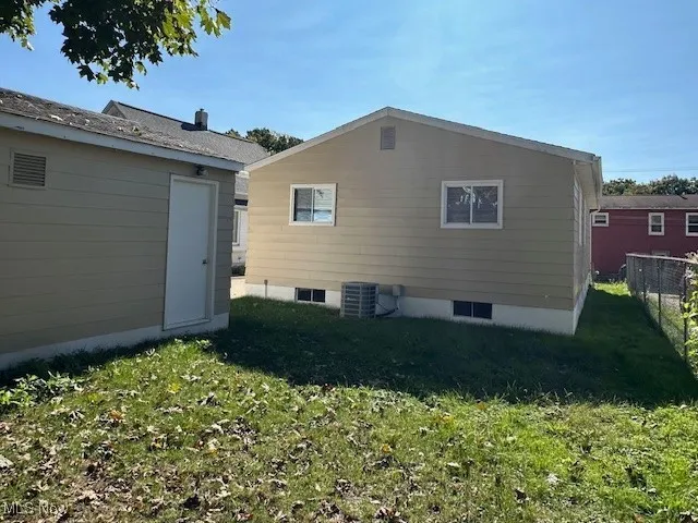 Rear view of house with central air condition unit and a lawn