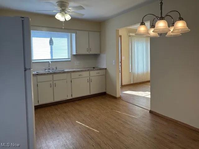 Kitchen with white cabinetry, sink, fridge, and hanging light fixtures