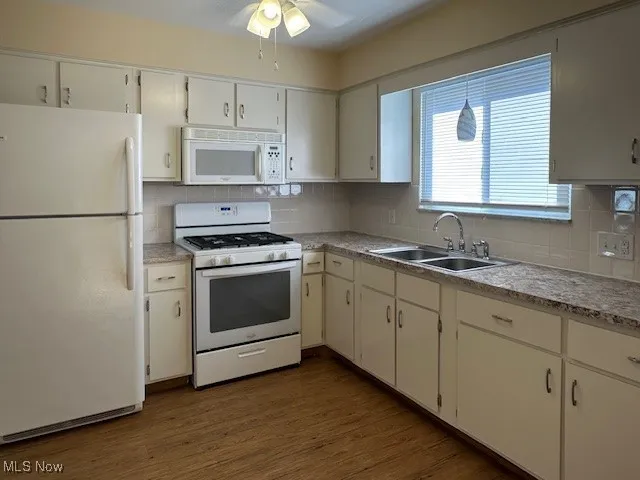 Kitchen featuring refrigerator, sink, stove, white cabinetry, and dark hardwood / wood-style flooring