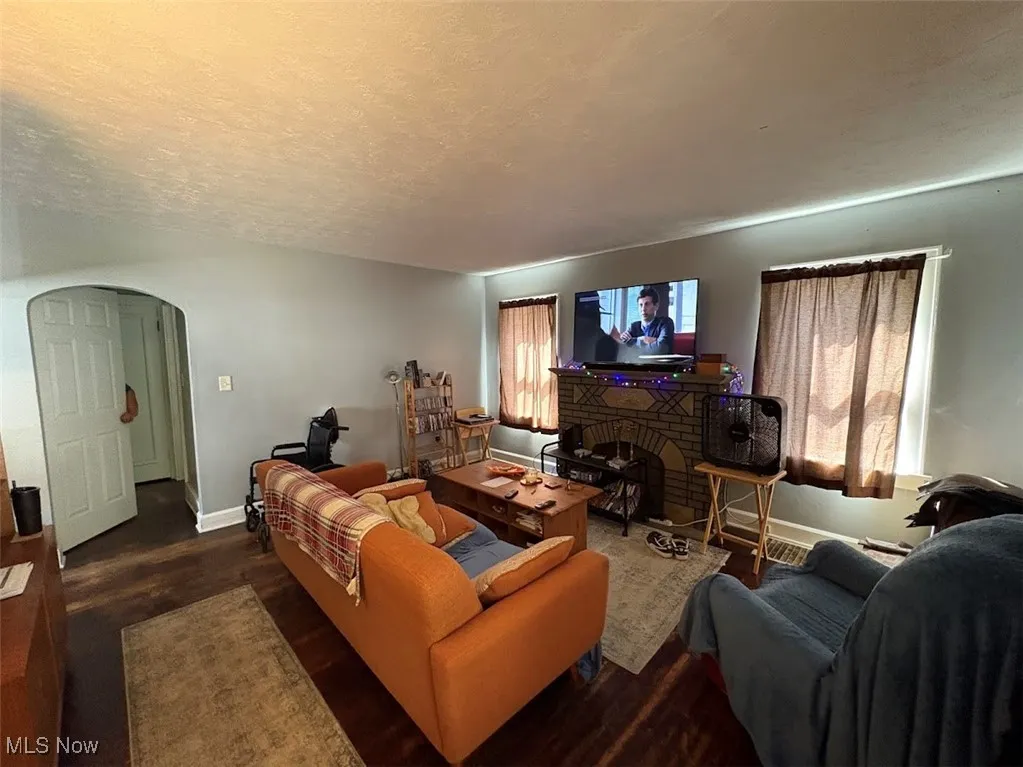 Living area with arched walkways, dark wood-style flooring, a textured ceiling, and a brick fireplace