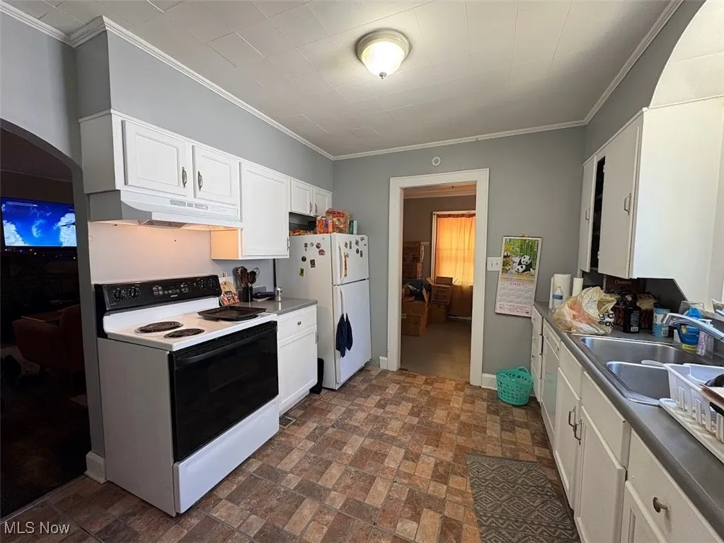 Kitchen with white cabinetry, white appliances, arched walkways, ornamental molding, and under cabinet range hood