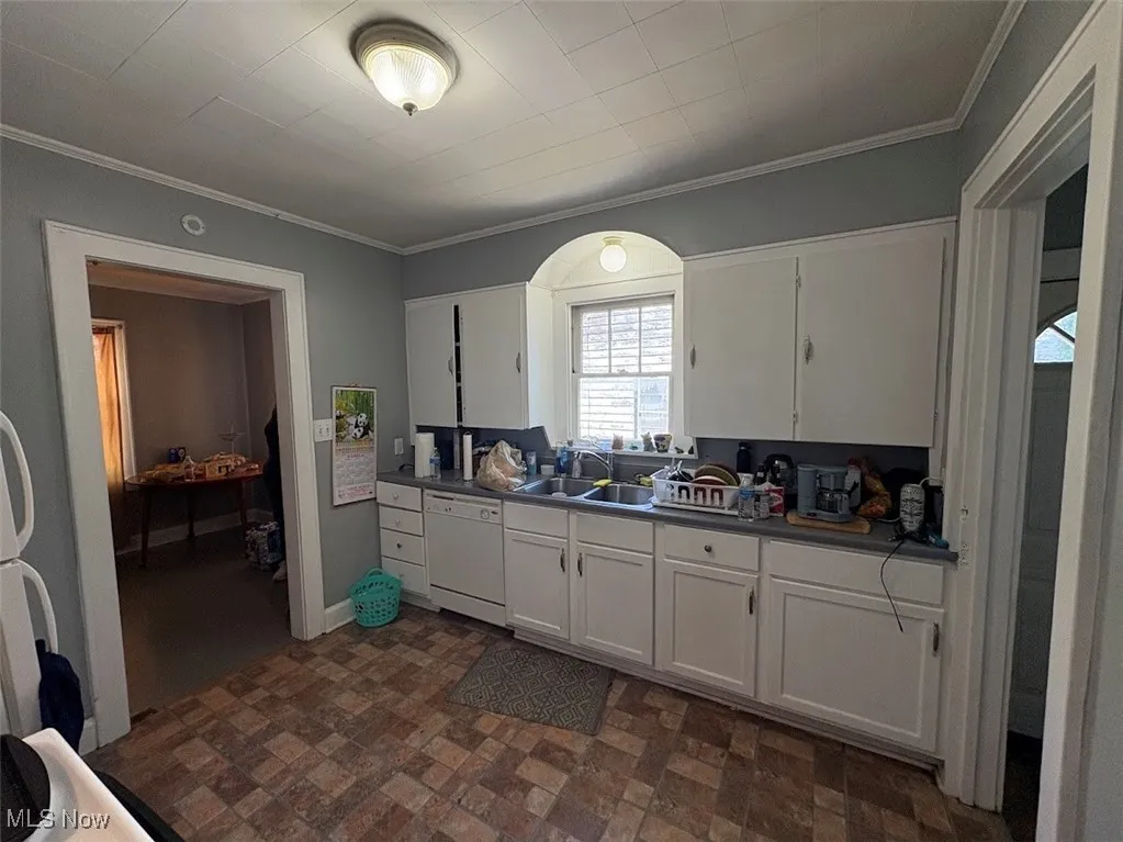 Kitchen featuring white cabinets, crown molding, white dishwasher, and dark countertops
