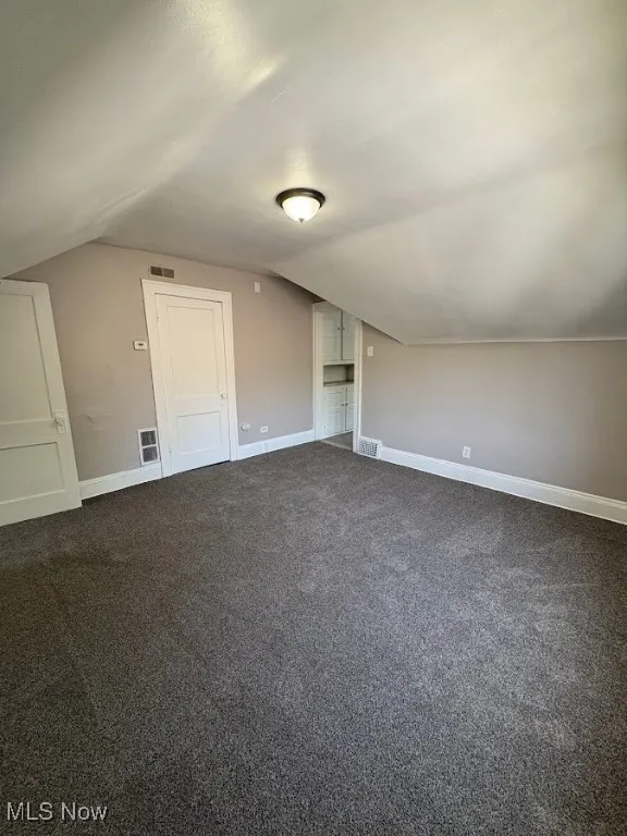 Bonus room with vaulted ceiling and dark carpet