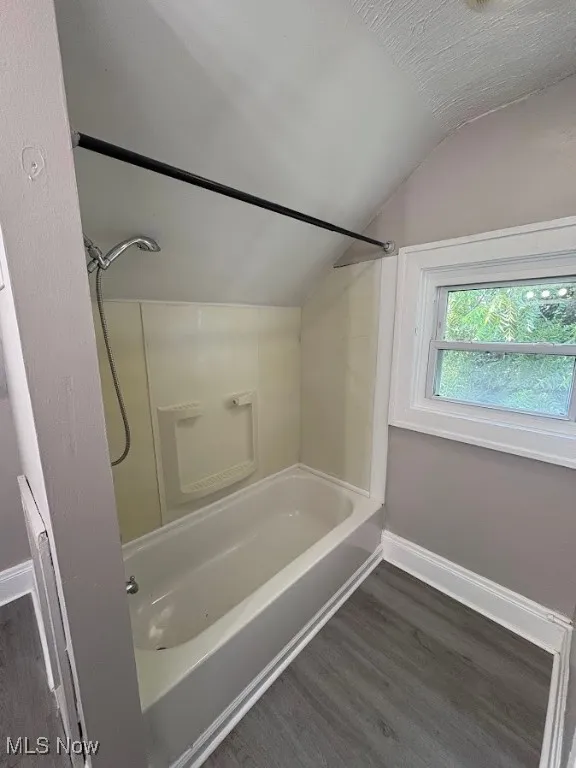 Full bathroom with dark wood-style floors, vaulted ceiling, and  shower combination