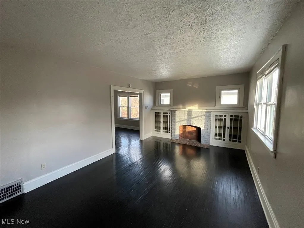 Unfurnished living room featuring a brick fireplace, dark wood-type flooring, and a textured ceiling