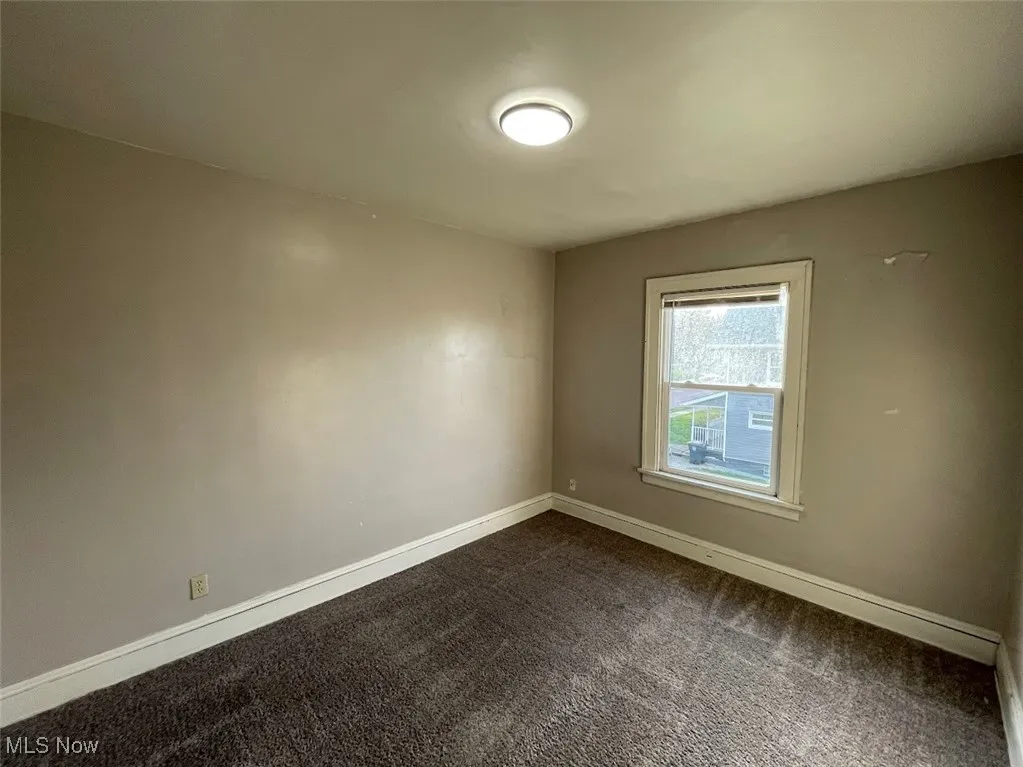 Empty room with dark colored carpet and baseboards
