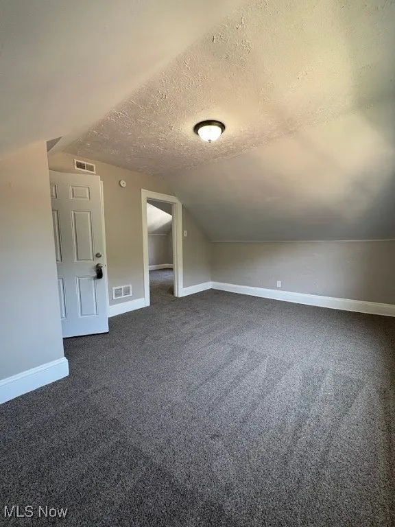 Bonus room with dark colored carpet, a textured ceiling, and vaulted ceiling