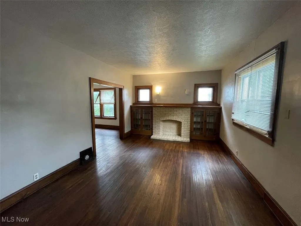 Unfurnished living room with dark wood finished floors, a fireplace, and a textured ceiling