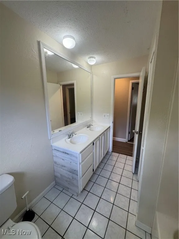 Full bath featuring a textured ceiling, light tile patterned floors, double vanity, and a textured wall