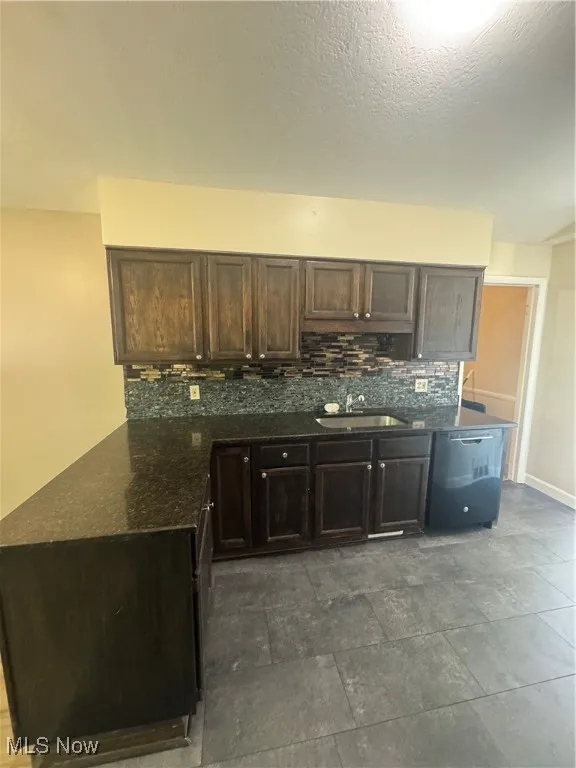 Kitchen with dark brown cabinetry, dark stone counters, decorative backsplash, and a textured ceiling