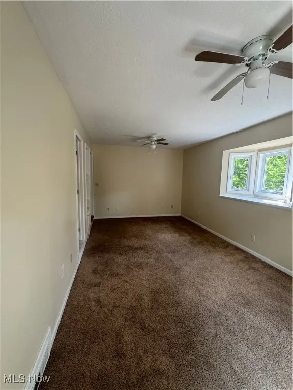 Spare room featuring dark carpet, a textured ceiling, and a ceiling fan