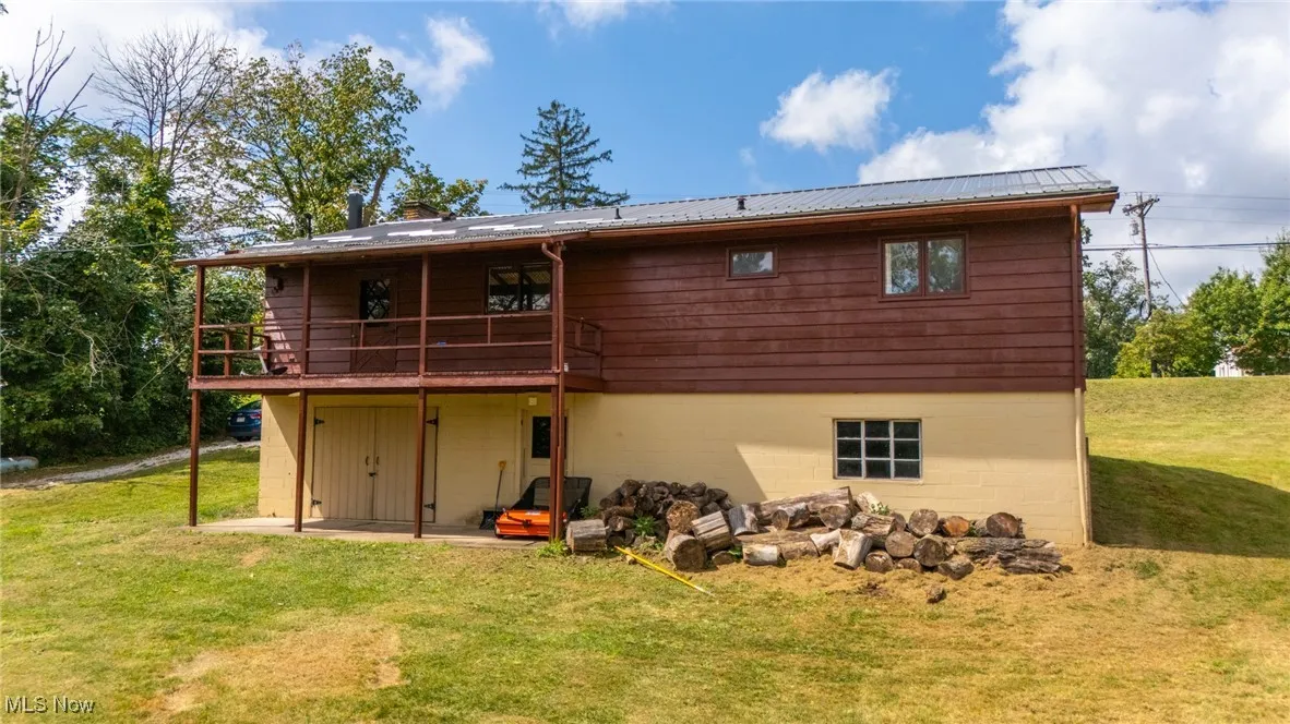 Back of house with a lawn, a wooden deck, a patio, a metal roof, and a chimney