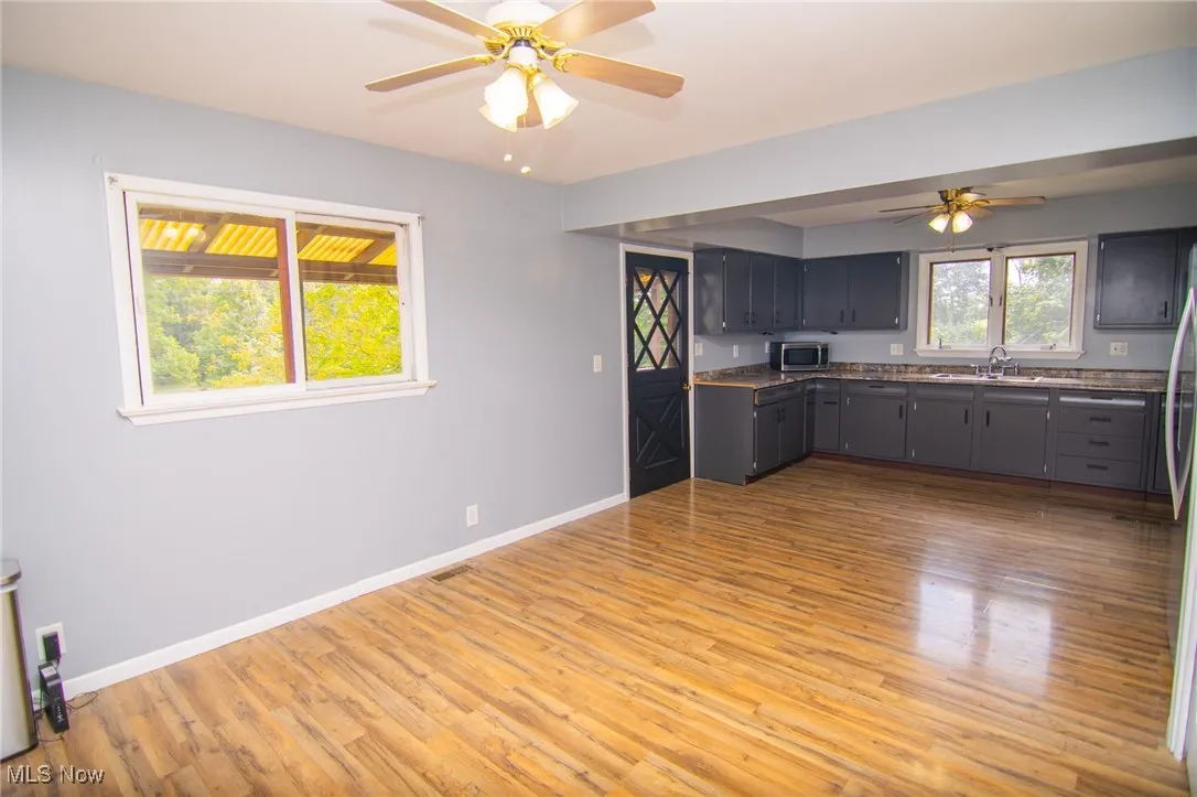 Kitchen featuring light wood-type flooring, a ceiling fan, dark countertops, gray cabinets, and stainless steel microwave