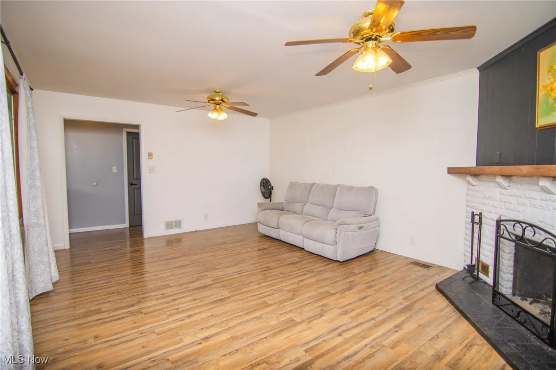 Living room featuring light wood-type flooring, a fireplace with raised hearth, ceiling fan, and ornamental molding
