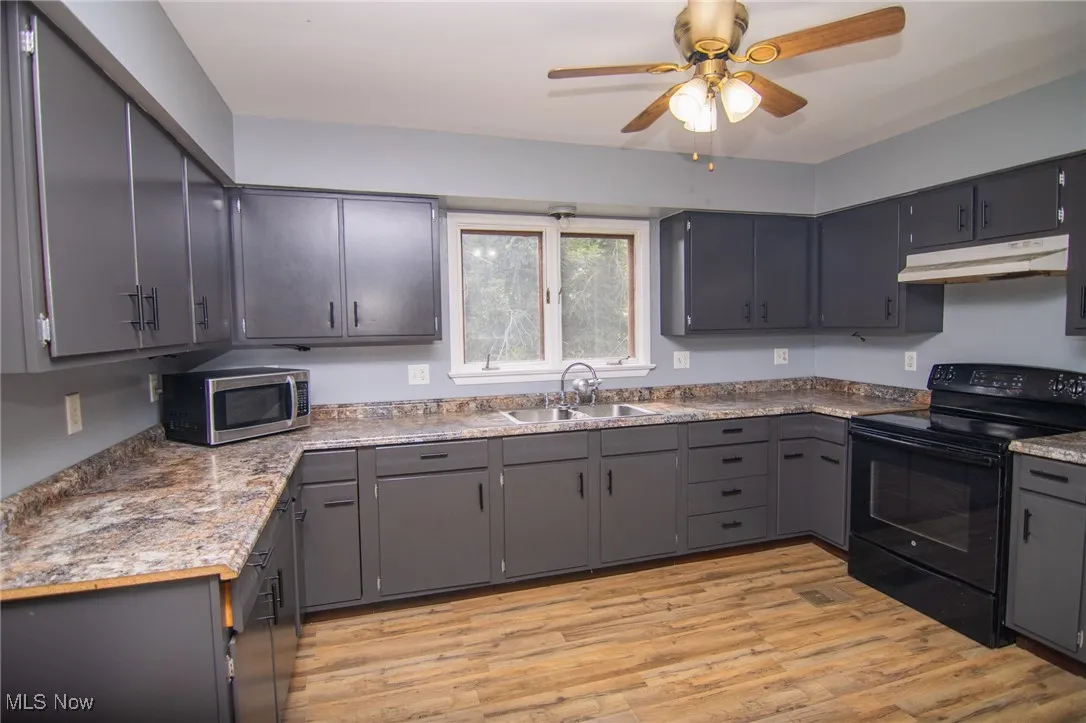 Kitchen with electric range, gray cabinets, light wood-type flooring, stainless steel microwave, and under cabinet range hood