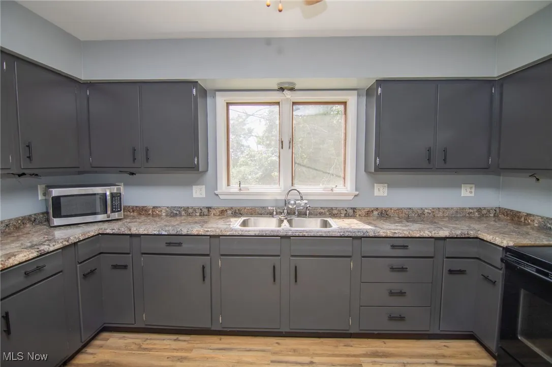 Kitchen with gray cabinets, black electric range oven, stainless steel microwave, and light wood-style flooring