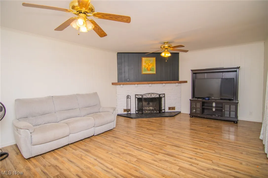 Living area with ornamental molding, light wood-style floors, a brick fireplace, and a ceiling fan