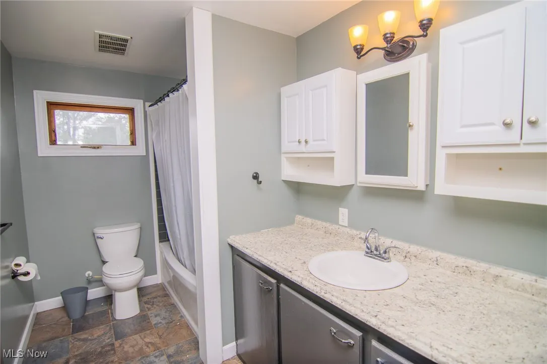 Full bath featuring vanity, shower / bath combo, and dark stone finish flooring