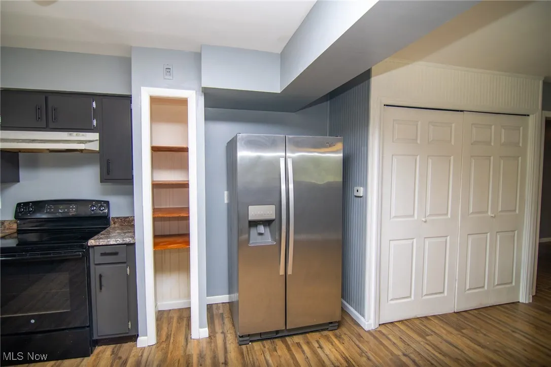 Kitchen with electric range, stainless steel fridge, dark wood-style flooring, under cabinet range hood, and gray cabinets