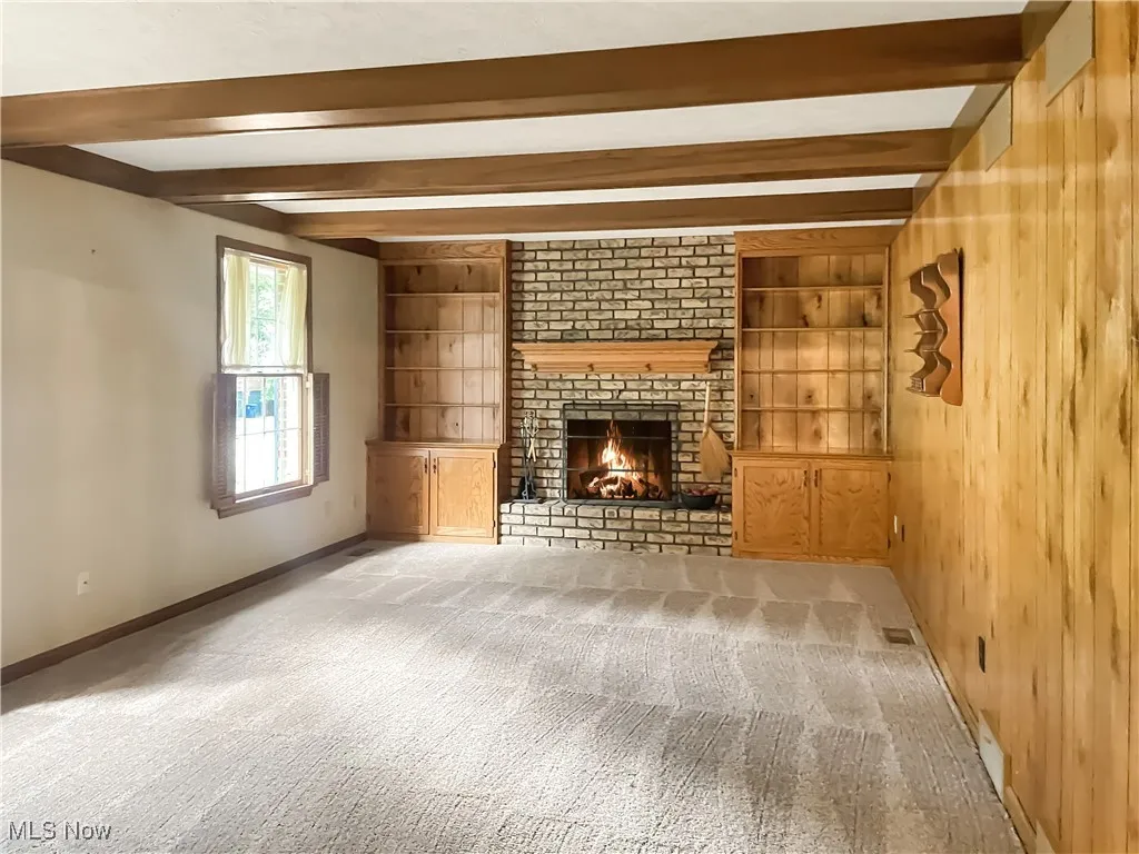 Unfurnished living room with beamed ceiling, built in features, a brick fireplace, and carpet flooring