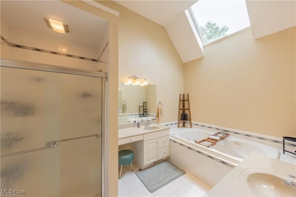 Bathroom featuring a stall shower, vanity, a bath, light tile patterned flooring, and a skylight
