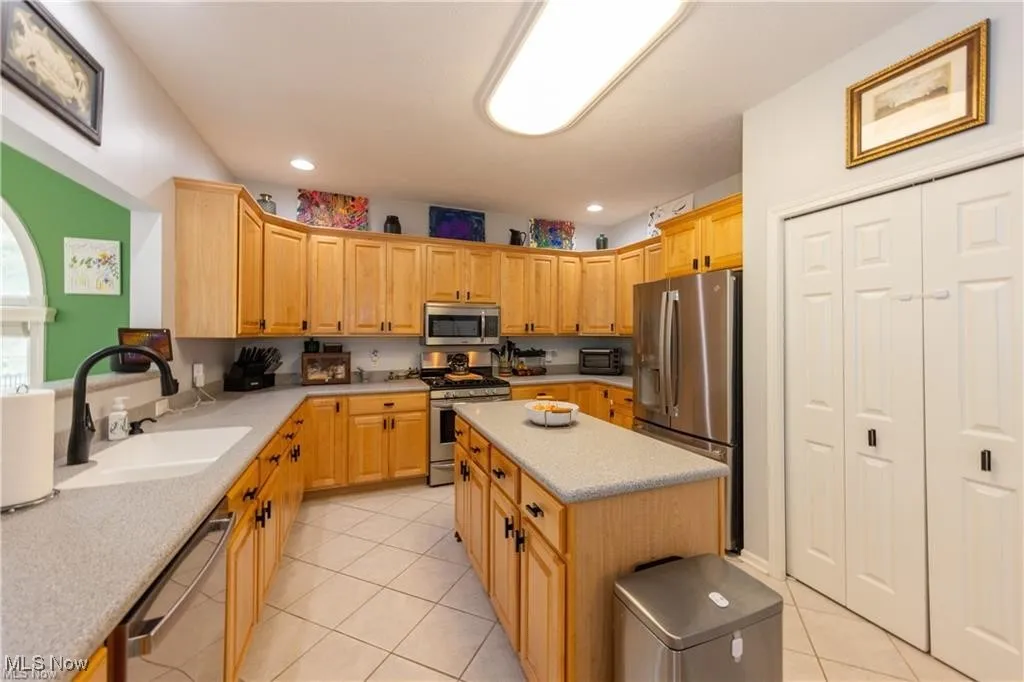 Kitchen featuring stainless steel appliances, light tile patterned flooring, a center island, light brown cabinets, and recessed lighting