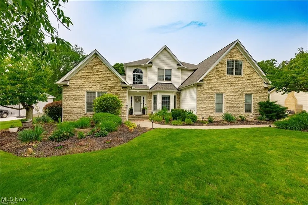 View of front of home featuring stone siding, a front yard, and roof with shingles