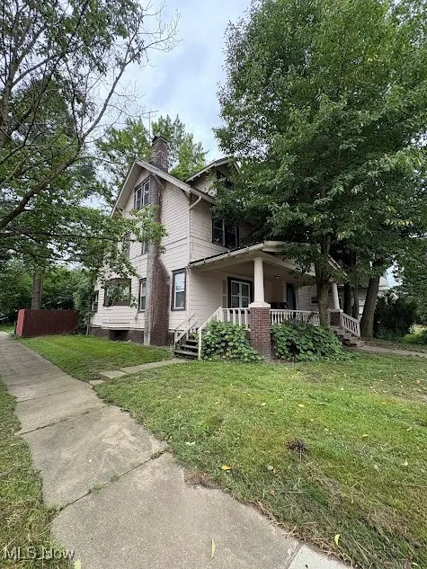 View of side of property with covered porch, a chimney, and a yard