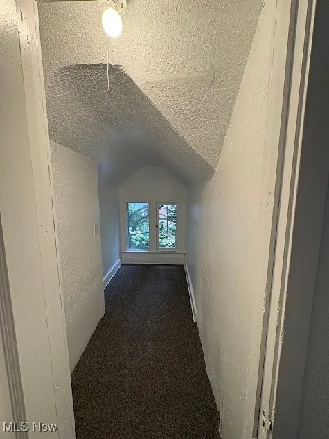 Bonus room featuring a textured wall, lofted ceiling, a textured ceiling, and dark colored carpet