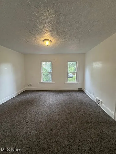 Unfurnished room featuring dark colored carpet and a textured ceiling