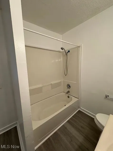Full bathroom featuring dark wood-style flooring, shower / bathtub combination, and a textured ceiling