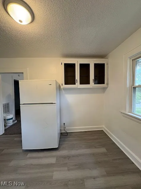 Kitchen featuring a textured ceiling, freestanding refrigerator, dark wood-style floors, and white cabinets